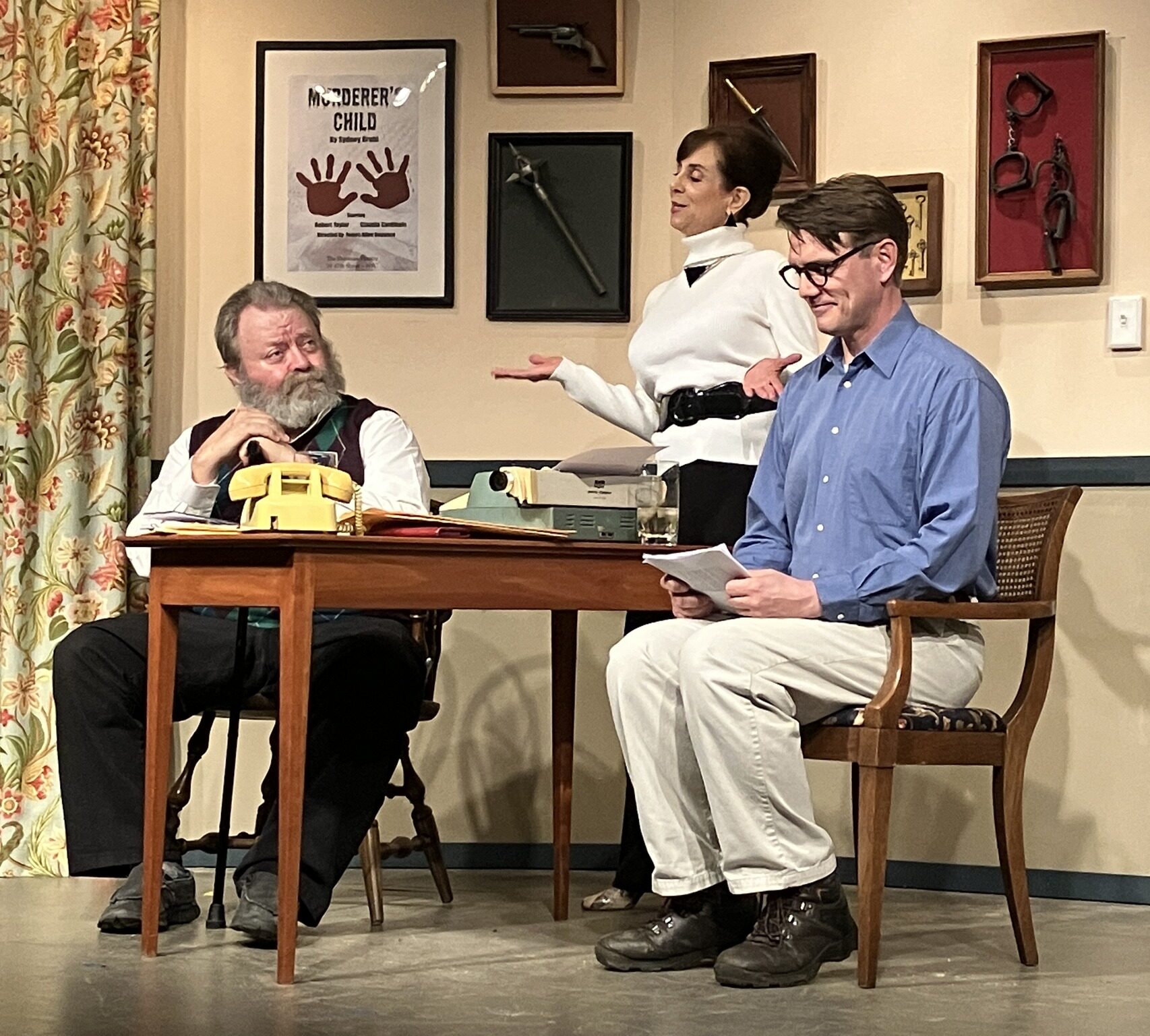 Three actors at a table on a stage